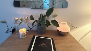 Et træbord med en indrammet bog med titlen 'MR MUDDY LION', en potteplante, to lysestager og et dekorativt spejl.