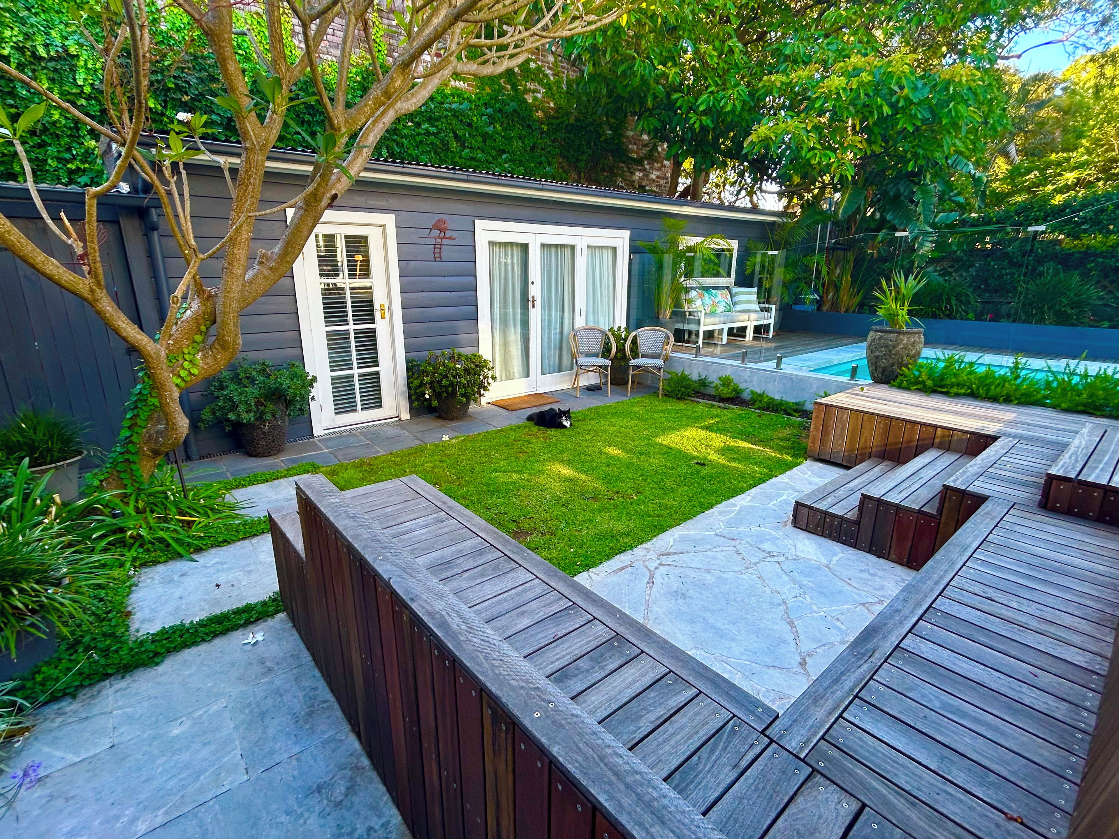 A backyard with a swimming pool, wooden deck, and a small lawn.
