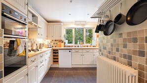 A modern kitchen with white cabinetry, a built-in oven, and a window with a view of greenery. - Spacious 4BR - Private driveway & Garden (Rutherglen)
