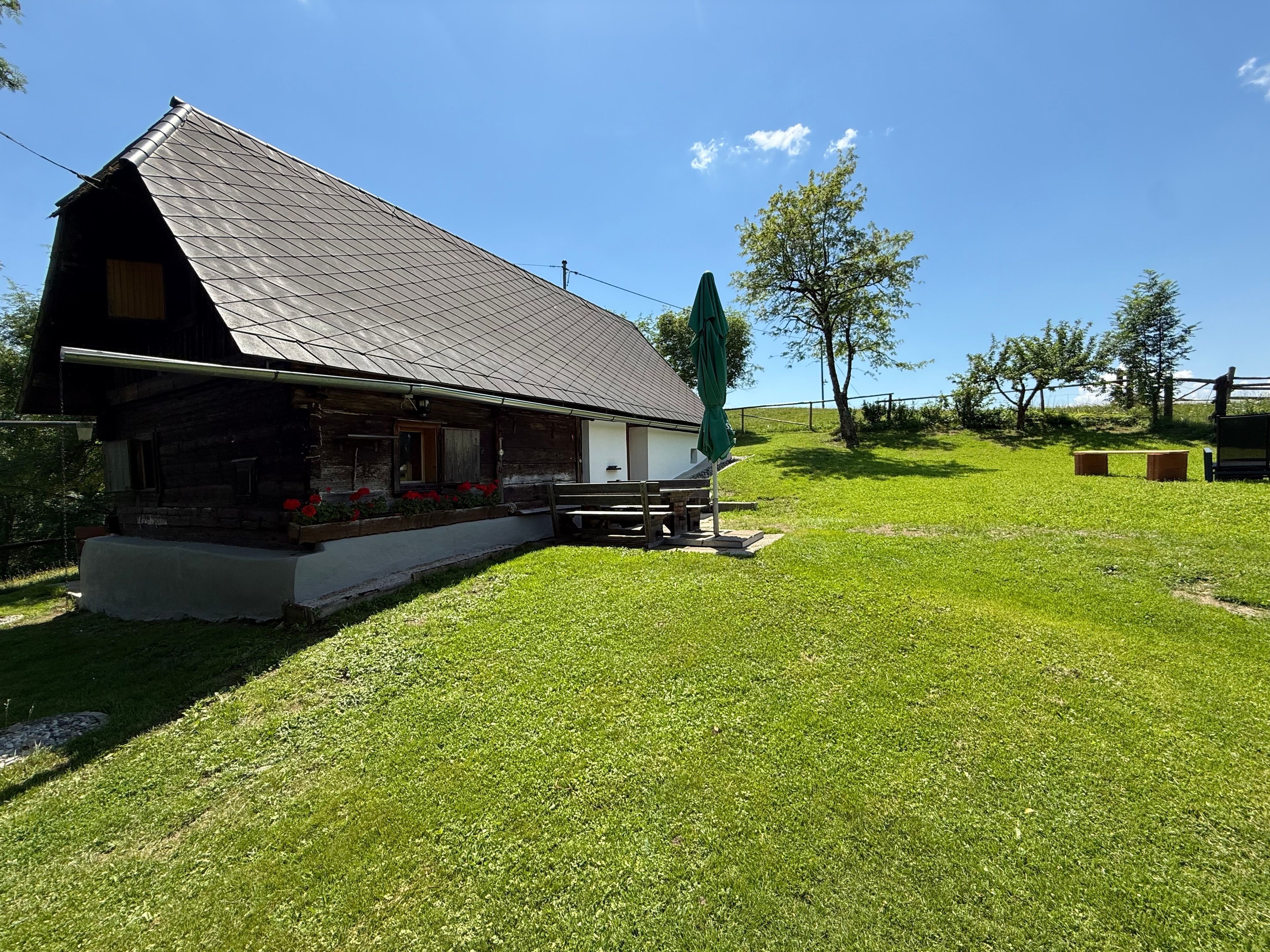 A rustic cabin with a sloped roof, a porch with a bench, and a small table.