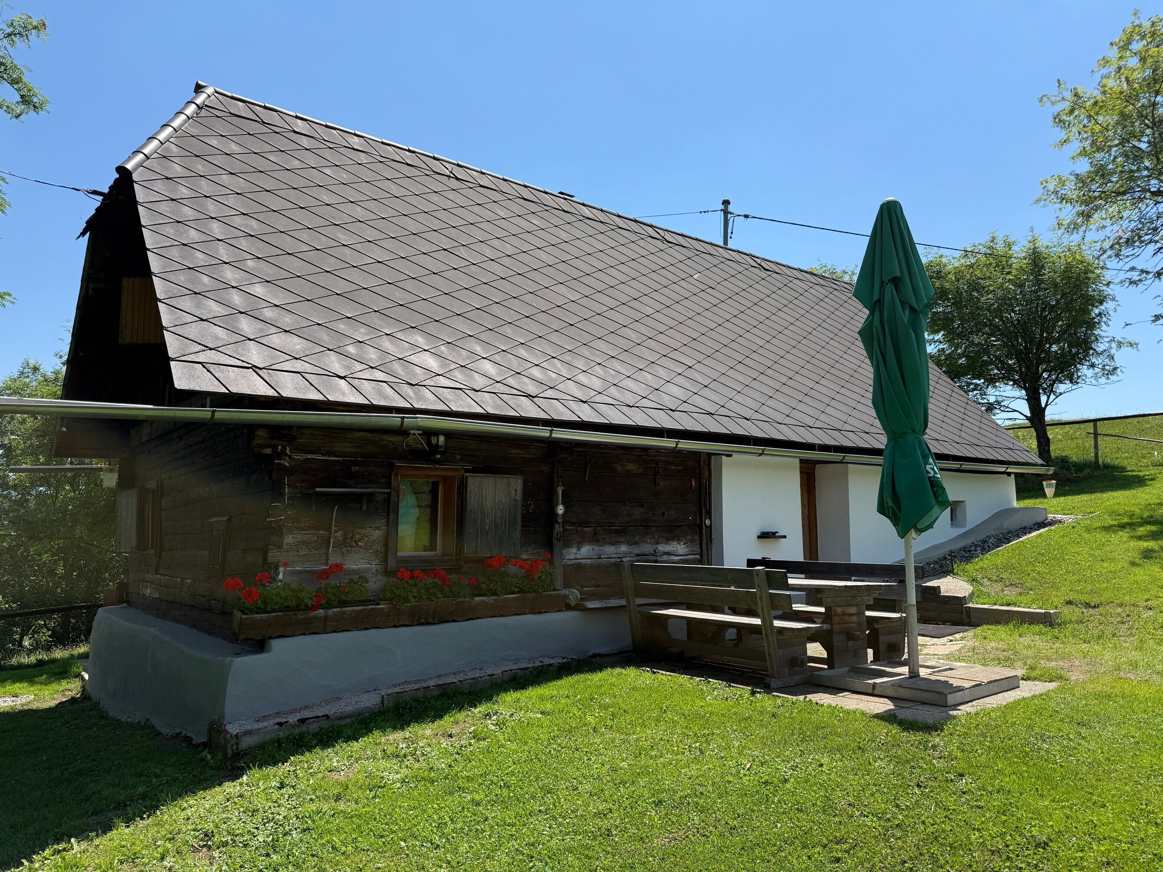 Een landelijk gebouw met een schuin dak, een houten veranda en een groene parasol.