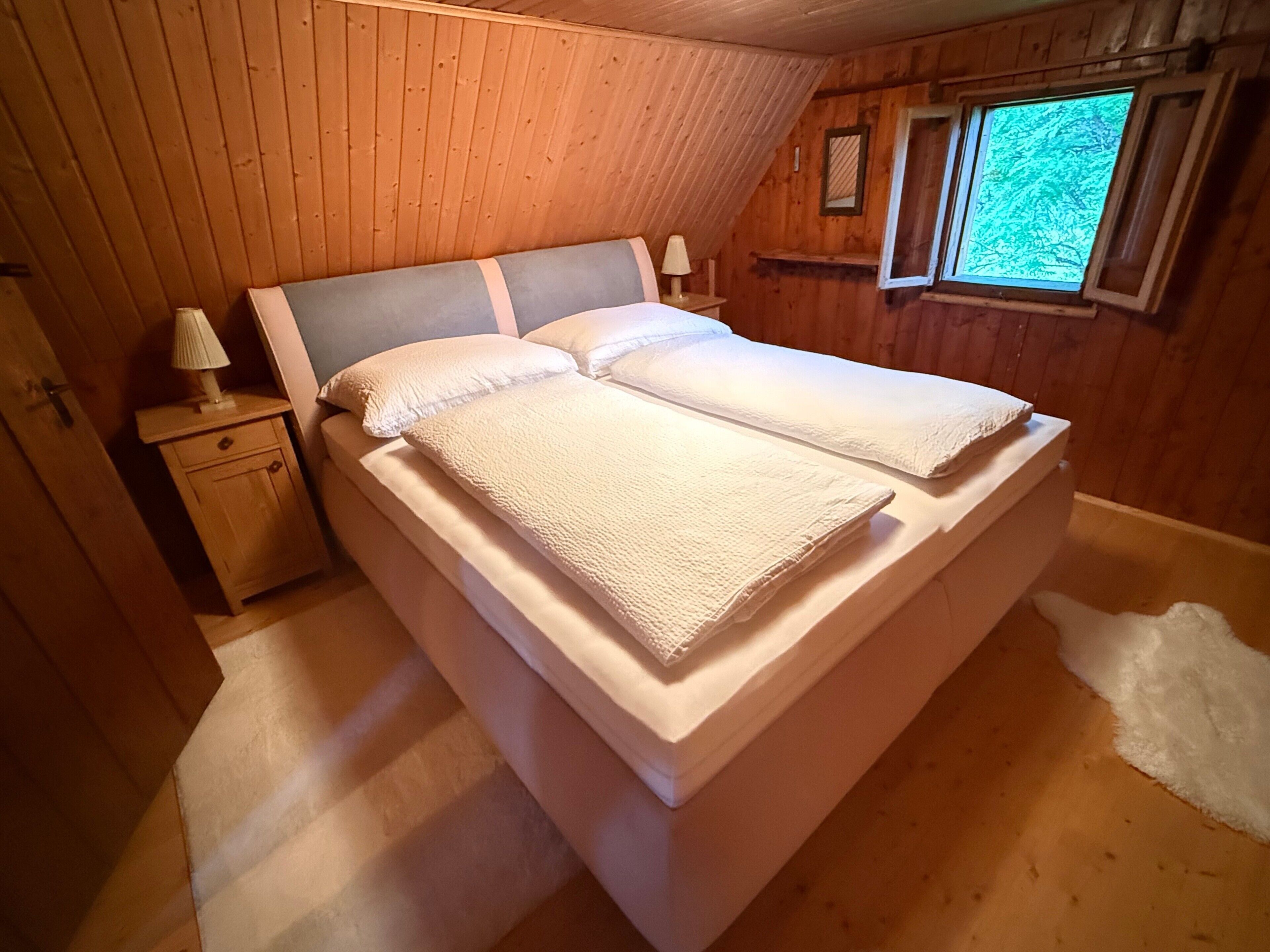 Een kamer met houten lambrisering, een bed, een nachtkastje en een raam.