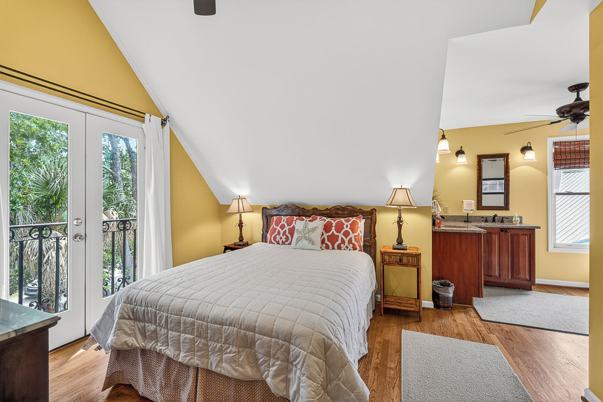 A bedroom with a large bed, a small desk, a bathroom, and a balcony with a railing.