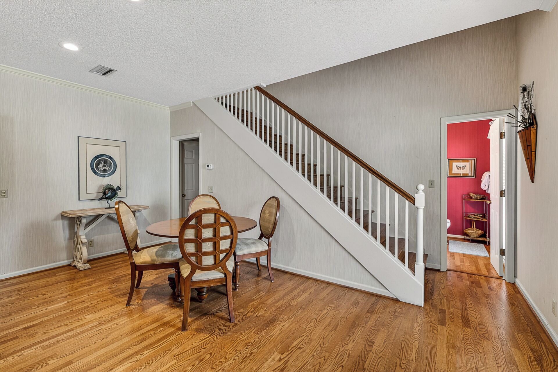 A dining area with a wooden table and chairs, a staircase, and a red accent wall.