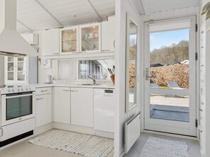 Eine moderne Küche mit weißen Schränken, einem Backofen, einer Spüle und einem Fenster mit Blick auf einen Garten.
