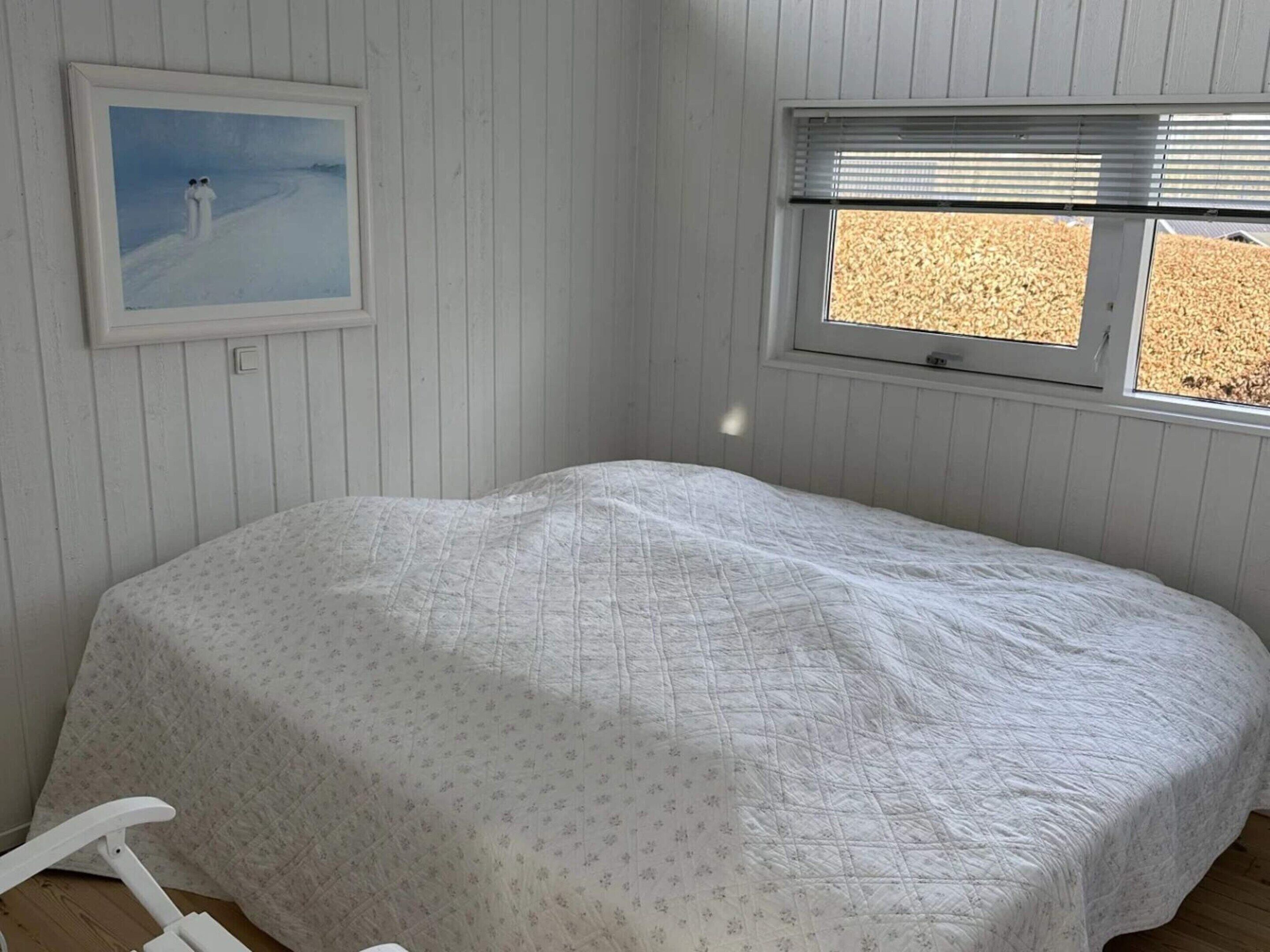 A room with a bed, a window, and a framed painting on the wall.