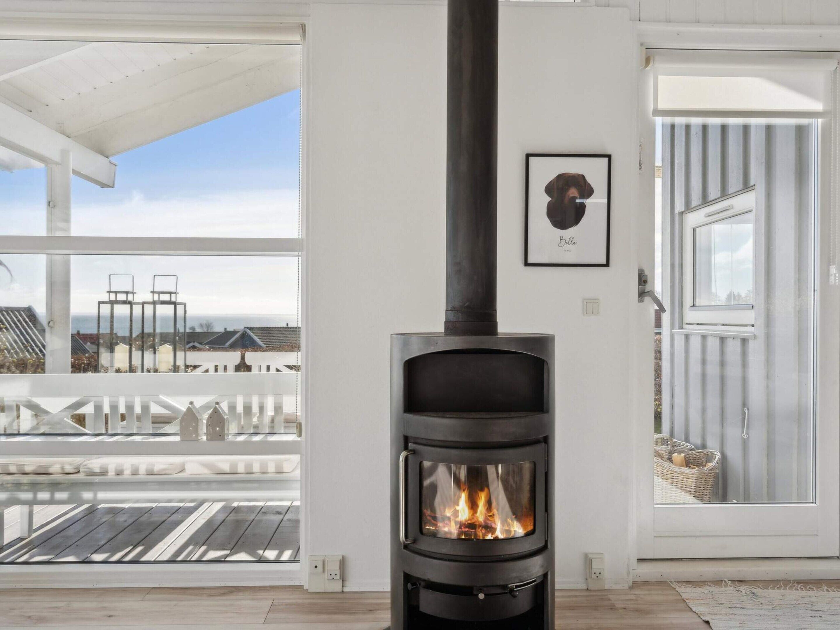 A modern room with a wood-burning stove, a white ceiling, and a view of the cityscape through large windows.