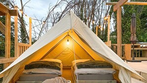 Tienda con dos camas, un farol y una cesta tejida sobre una terraza de madera.