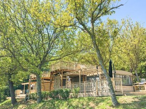 A wooden cabin with a deck and multiple levels, surrounded by trees.