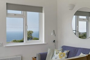 A room with a large window, a round mirror, and a bed with a quilted cover. - Kitticarn, Panoramic Sea Views, Garden, Parking (Sennen)