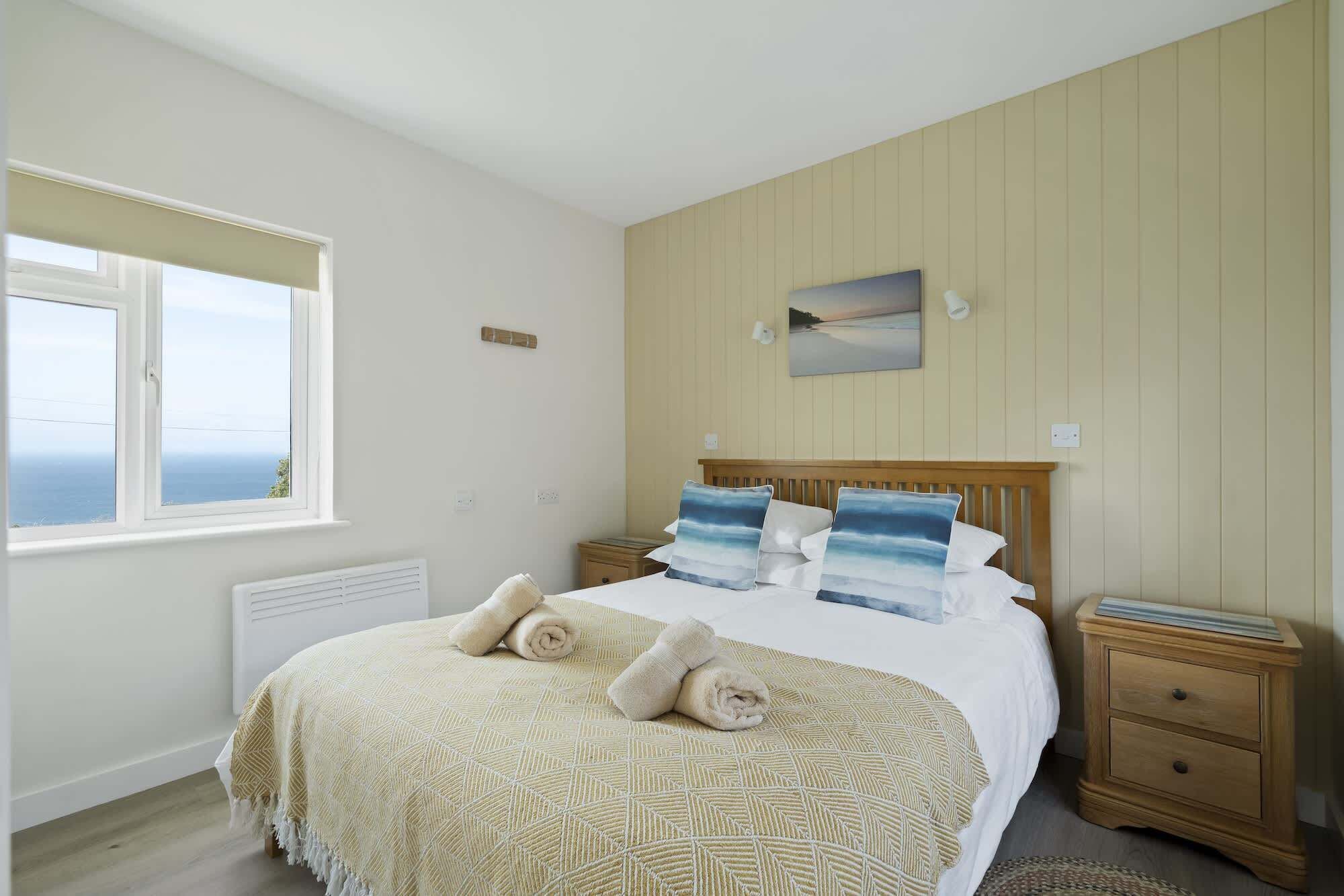 A bedroom with a bed, two bedside tables, a window with a view, a wall-mounted picture, and a radiator.