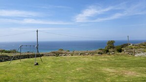 A grassy field with a swing set, a stone wall, and a view of the ocean. - Kitticarn, Panoramic Sea Views, Garden, Parking (Sennen)