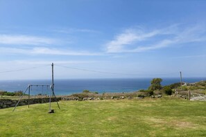 A grassy field with a swing set, a stone wall, and a view of the ocean. - Kitticarn, Panoramic Sea Views, Garden, Parking (Sennen)