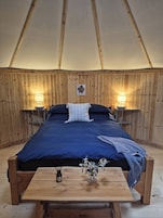 Una habitación con carpa que tiene una cama, lámparas de noche, una mesa de madera y un jarrón con flores.