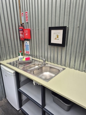 A kitchenette with a sink, a fire extinguisher, a fire blanket, a framed picture, and a small refrigerator. - Unique Retreat, Sleeps 2 With Hot Tub & Pets Ok (Glengarriff)