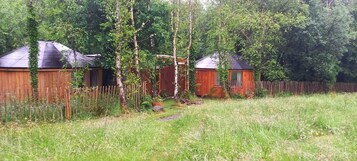 Una cabaña de madera con techo de metal, rodeada por una cerca de madera y árboles.
