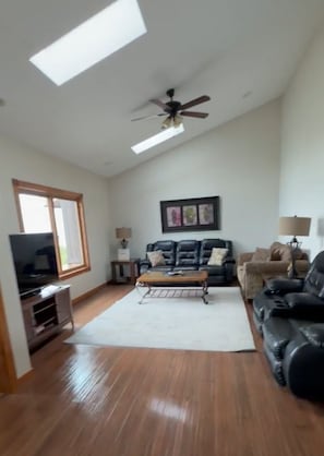 A spacious living room with a ceiling fan, a flat-screen TV, a sofa, and a coffee table. - Lake St. Helen Retreat with Pontoon, Kayaks, Hot Tub & Easy ORV Trail Access (St. Helen)