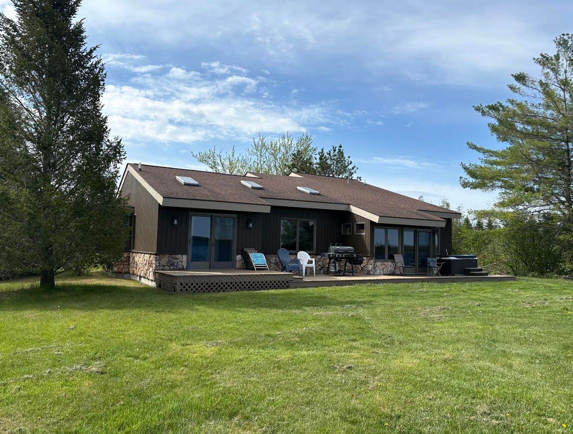 Ein modernes Haus mit überdachter Terrasse, Grill und Rasen.
