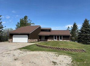 A two-story house with a garage, a sloped roof, and a stone foundation. - Lake St. Helen Retreat with Pontoon, Kayaks, Hot Tub & Easy ORV Trail Access (St. Helen)
