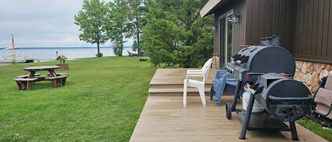 Eine Terrasse mit Grill, Picknicktisch und Stühlen mit Blick auf einen See.