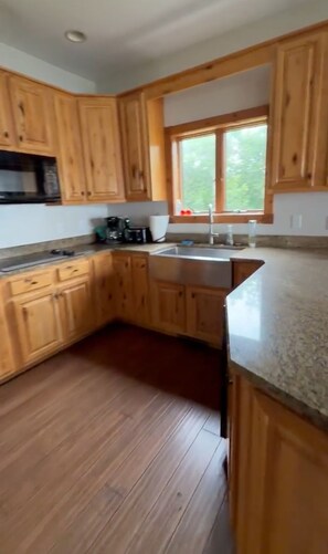 A kitchen with wooden cabinets, a stainless steel sink, and a window providing natural light. - Lake St. Helen Retreat with Pontoon, Kayaks, Hot Tub & Easy ORV Trail Access (St. Helen)
