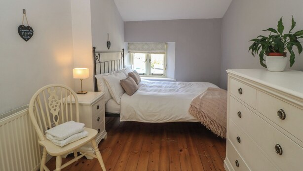 A bedroom with a bed, a chair, a dresser, a bedside table, a lamp, a window, and a plant. - 2 The Gardens (Lechlade)