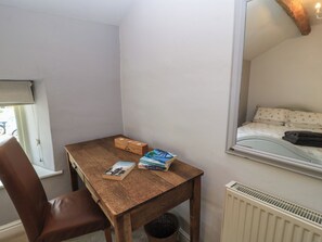 Ein Zimmer mit einem Holztisch, einem Stuhl, einem Heizkörper und einem Fenster mit Blick auf ein Bett.
