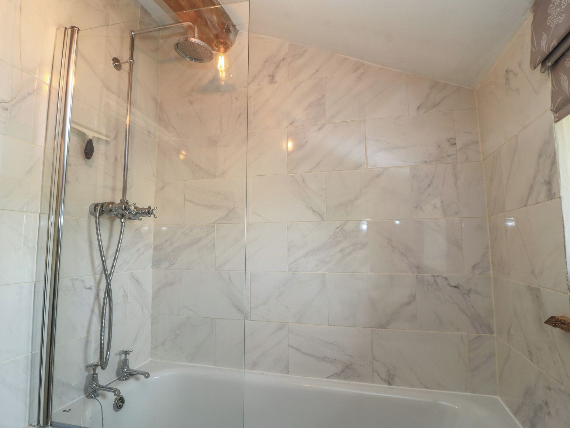 A bathroom with a glass-enclosed shower, a bathtub, and marble tiles.