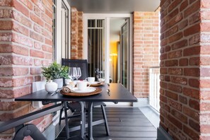 Ein Tisch für zwei Personen mit einem Topfpflanzen, weißen Tassen und einem Weinglas auf einem Balkon mit Ziegelwänden.