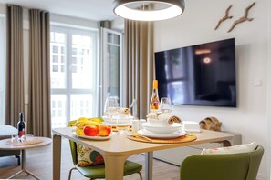 Ein Esstisch gedeckt mit Früchten, Gläsern und einer Flasche, in einem Raum mit Fernseher und Vorhängen.