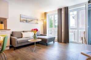 Ein modernes Wohnzimmer mit einem grauen Sofa, einem kleinen runden Tisch mit Blumenvase und einem Bild an der Wand.