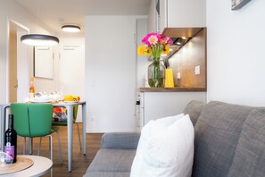En moderne stue med en grå sofa, et spisebord med stole, og et køkkenområde med et træskab.
