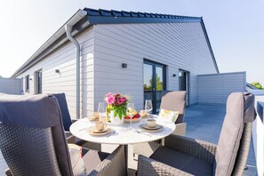 A modern house with a sloped roof, a balcony with outdoor furniture, and a dining table set for two. - Heart of Kellenhusen 18 - Penthouse vacation. Sauna. Roof terrace. (Kellenhusen)