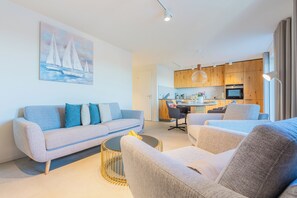 Ein modernes Wohnzimmer mit einer Couch, Sesseln, einem Couchtisch und einem Segelbootgemälde an der Wand.