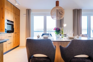 A modern kitchen with wooden cabinets, a built-in oven, and a dining area with a table set for two. - Heart of Kellenhusen 18 - Penthouse vacation. Sauna. Roof terrace. (Kellenhusen)