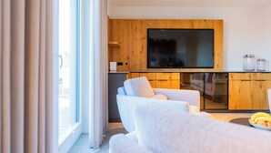 Een moderne woonkamer met een bank, een flatscreen televisie bevestigd aan een houten wand, en een eethoek met een glazen kast.