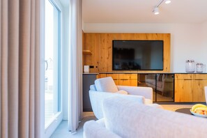 Ein modernes Wohnzimmer mit einer Couch, einem flachbildfernseher, der an einer Holzwand angebracht ist, und einem Essbereich mit einer Glasvitrine.