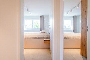 A modern bedroom with two beds, a window, and a wooden door. - Heart of Kellenhusen 18 - Penthouse vacation. Sauna. Roof terrace. (Kellenhusen)