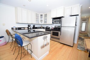 A kitchen with white cabinets, a black countertop, a stainless steel refrigerator, and a built-in oven. - Beachcrest 8 - Ocean City, MD (Ocean City)