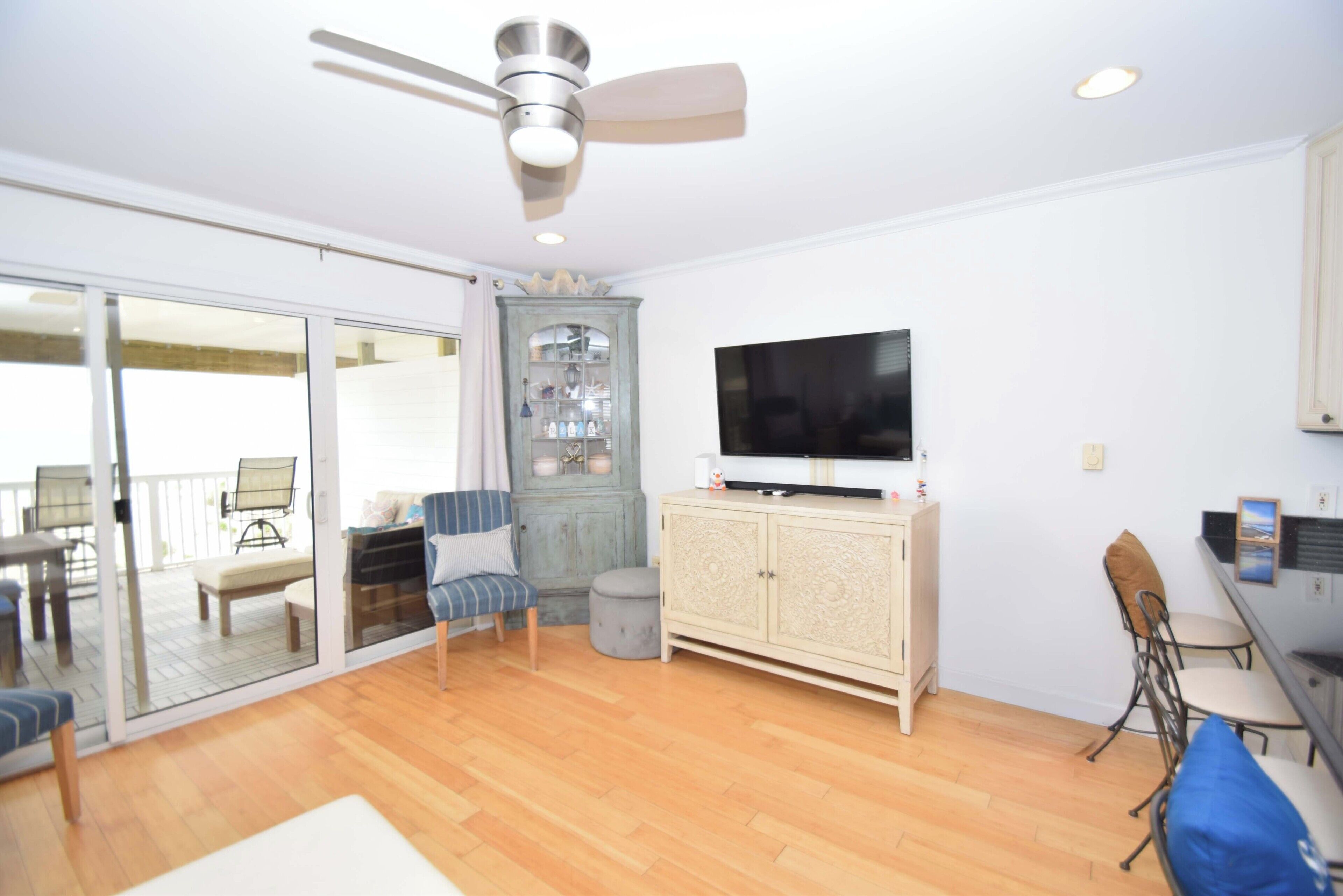 A spacious room with a sliding glass door leading to an outdoor area, a ceiling fan, a flat-screen TV, and a cabinet.