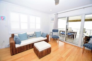 A room with a wicker sofa, a matching ottoman, a striped chair, and a dining table with chairs. - Beachcrest 8 - Ocean City, MD (Ocean City)