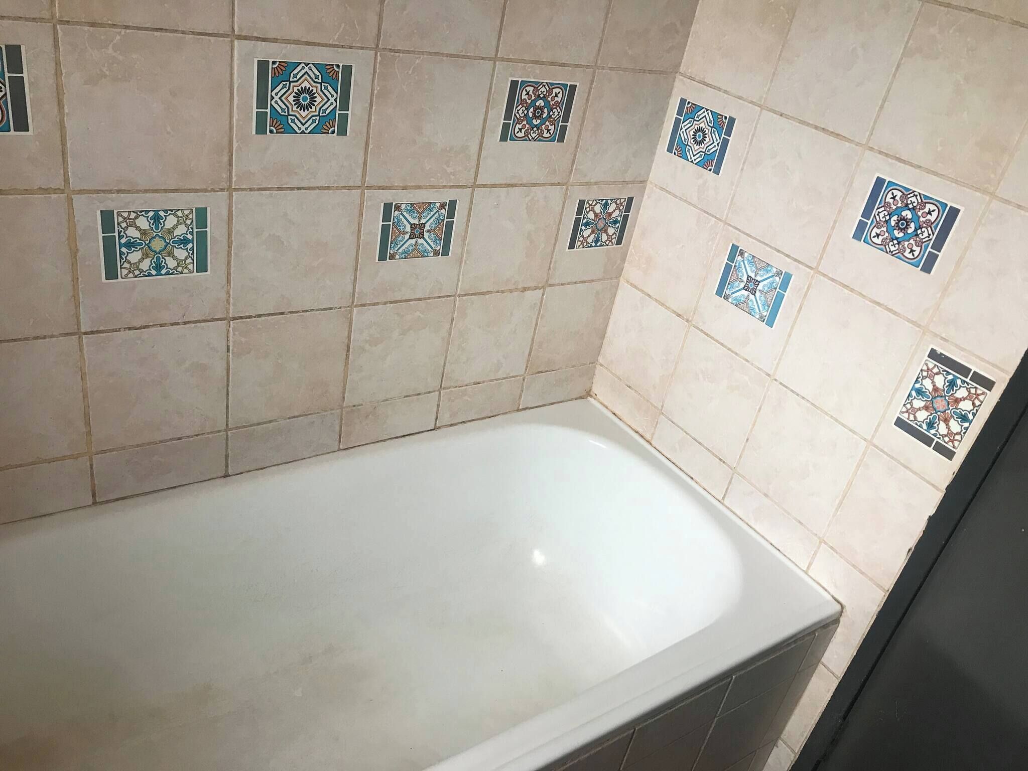 Une salle de bain avec une baignoire blanche, des carreaux de couleur beige et des carreaux décoratifs aux motifs géométriques.