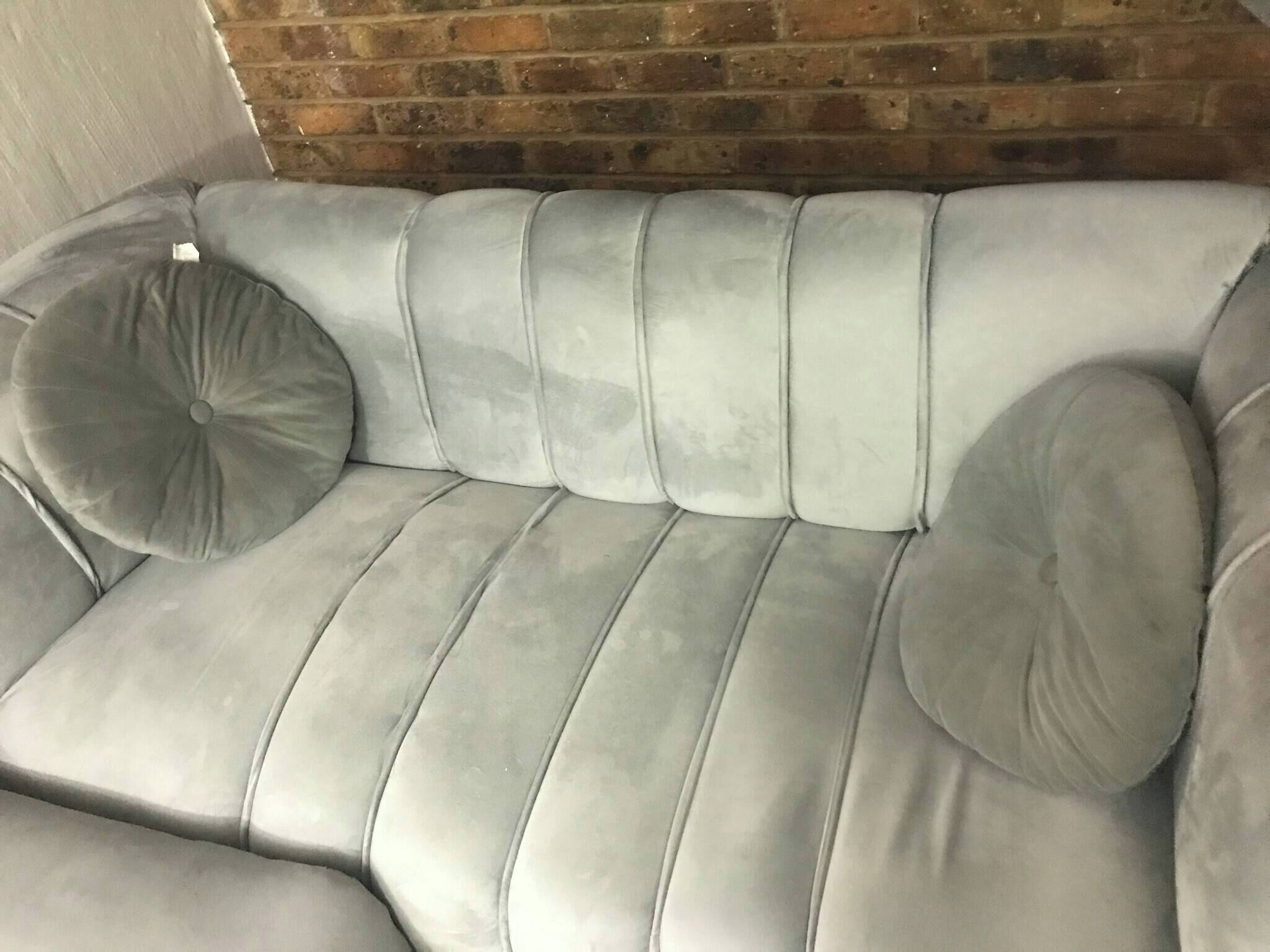 A grey upholstered sofa with a brick wall behind it.