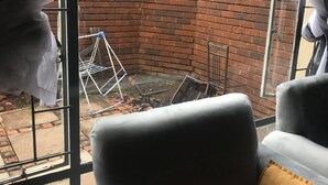 Una habitación con vista a un muro de ladrillo, una silla de metal y una ventana con cortinas translúcidas.
