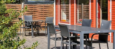 Une terrasse en bois avec une table et des chaises, un bâtiment rouge doté de fenêtres et une clôture en bois.