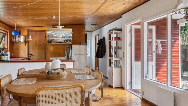 A cozy kitchen with wooden cabinets, a dining table with chairs, and a view through an open door. - 5 Star Holiday Home in Gedser (Gedser)