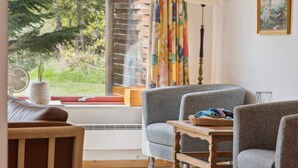 A cozy living room with a sofa, armchairs, a wooden table, a fan, and a window with curtains. - 5 Star Holiday Home in Gedser (Gedser)