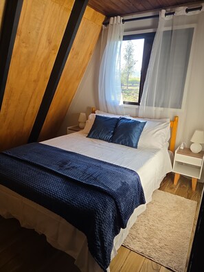 A bedroom with a bed, bedside tables, a window with curtains, and a view of greenery outside.