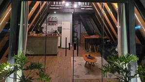 A triangular-roofed structure with a visible kitchen area, wooden flooring, and potted plants. - A retreat at Chalé A-Frame Parobé, with a lake, fire pit, and grill. (Poço Fundo)