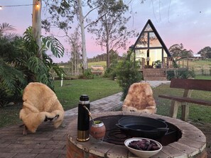 A patio with a fire pit, a bottle, and a bowl of charcoal. - A retreat at the Parobé A-Frame Chalet, featuring a lake, a fire pit, and a grill. (Poço Fundo)